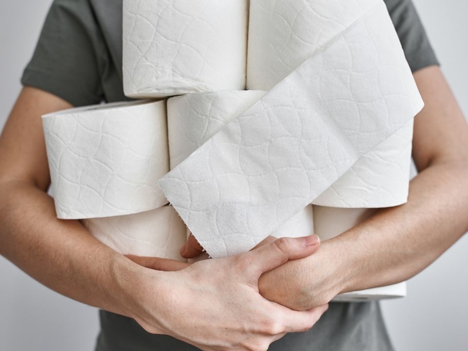 Homem carregando no braço uma pilha de Papel Higiênico 100% Celulose Folha Dupla da JA PAPER.